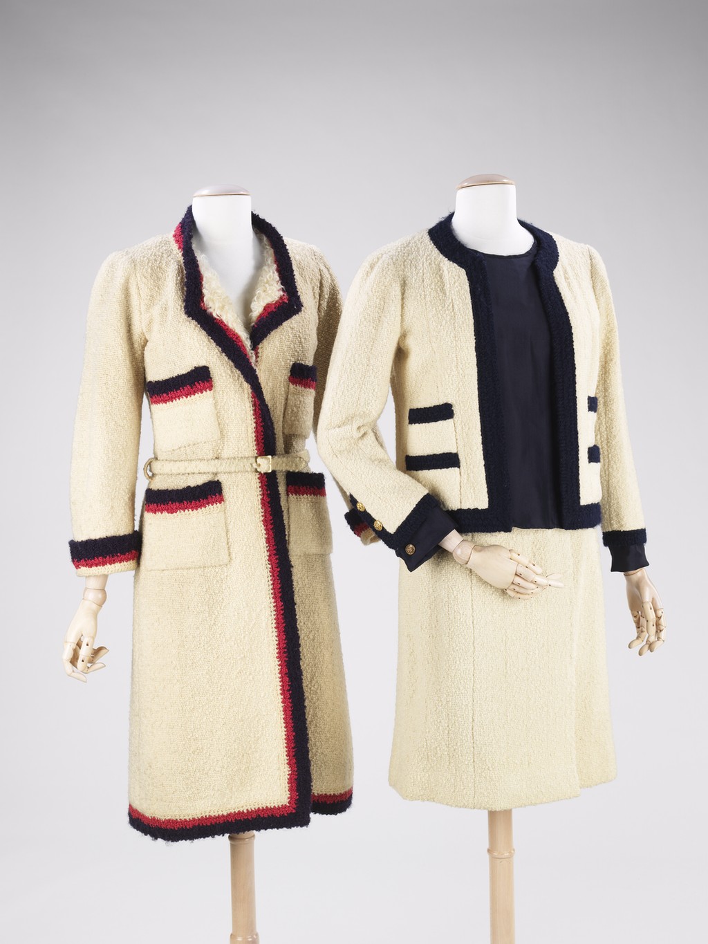 Here is a photo of two outfits Chanel designed from the mid-twentieth century. The piece on the left is a longer, belted coat with multi-colored trim. On the right is one of Chanel’s classic suits with navy trim.
