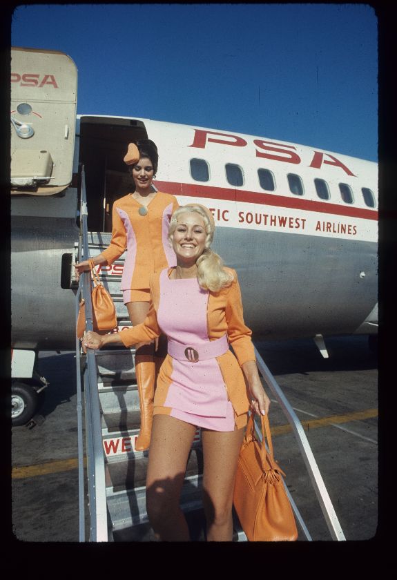 Two female Pacific Southwest Airlines flight attendants are seen exiting an aircraft in their tight pink and orange dresses.