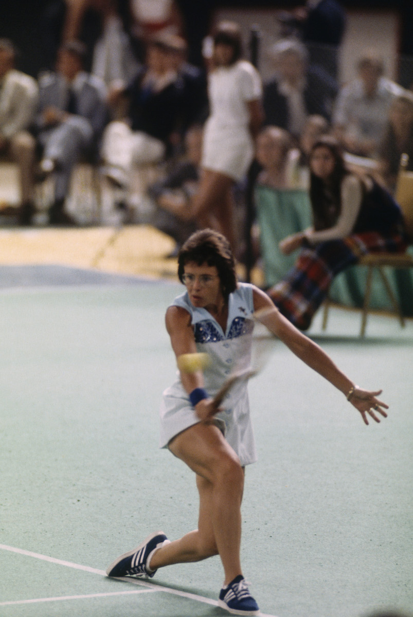 King is running across the court in her vibrant outfit going for a ball in the corner of the court.